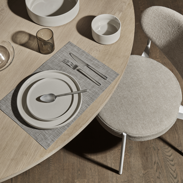 Elegant dining table setting with neutral plates and glassware on a textured placemat.