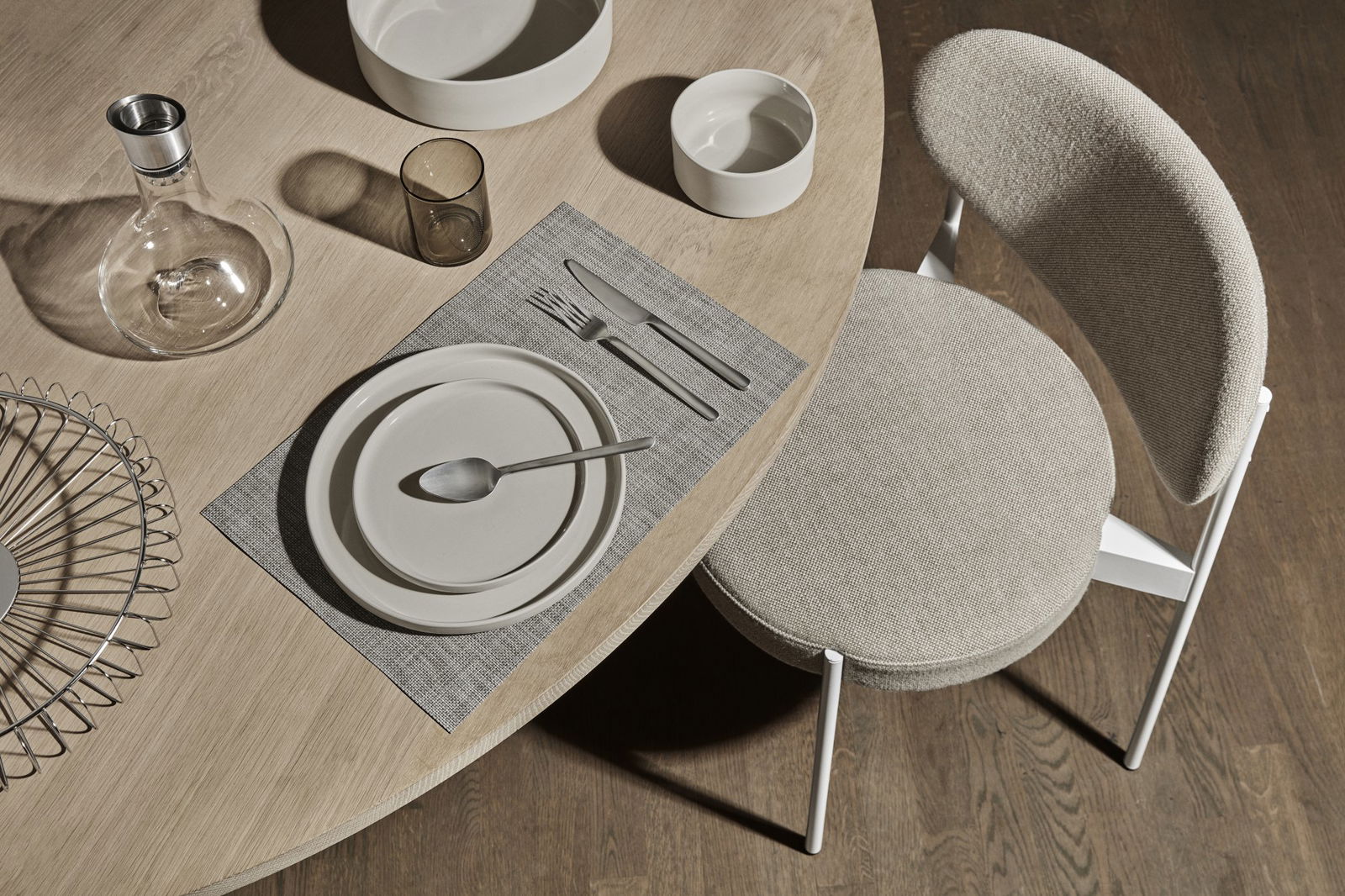 Elegant dining table setting with neutral plates and glassware on a textured placemat.