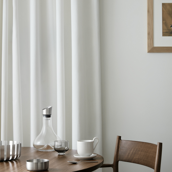Elegant dining setting with a wooden table, white curtains, and stylish glassware.