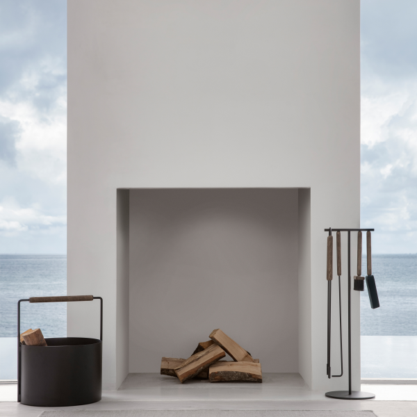 Moderner minimalistischer Kamin mit gestapeltem Holz und stilvollen Werkzeugen, mit Blick auf ruhige Gewässer.