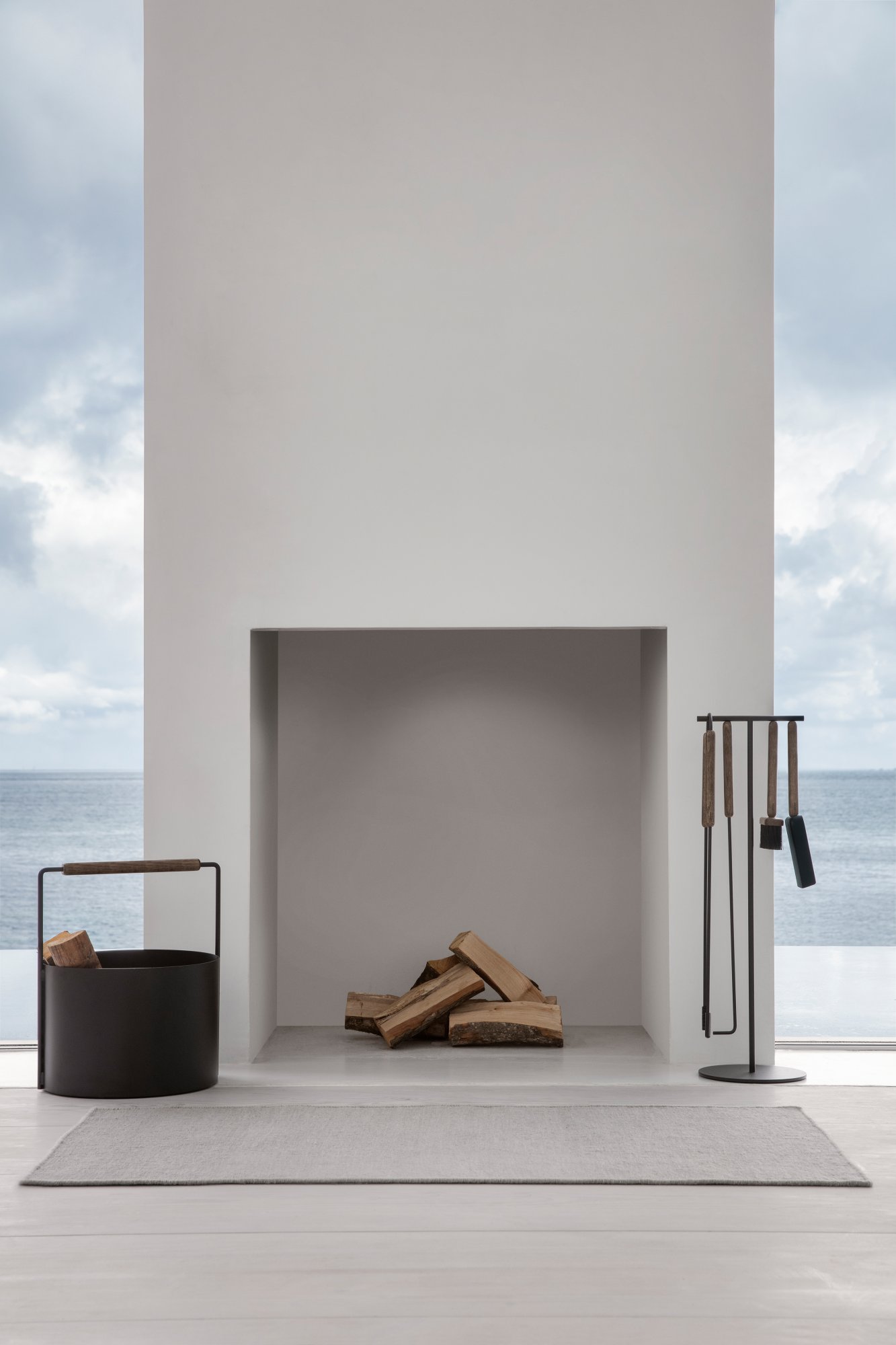 Moderner minimalistischer Kamin mit gestapeltem Holz und stilvollen Werkzeugen, mit Blick auf ruhige Gewässer.