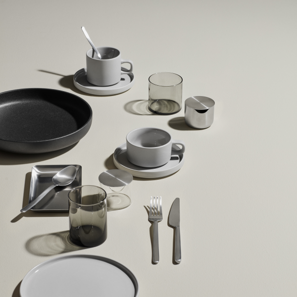 Moderner minimalistischer Esstisch mit Geschirr, Gläsern und Besteck auf einem neutralen Hintergrund.