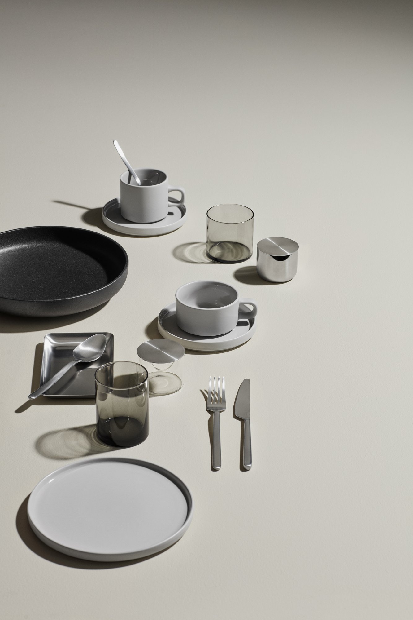 Moderner minimalistischer Esstisch mit Geschirr, Gläsern und Besteck auf einem neutralen Hintergrund.