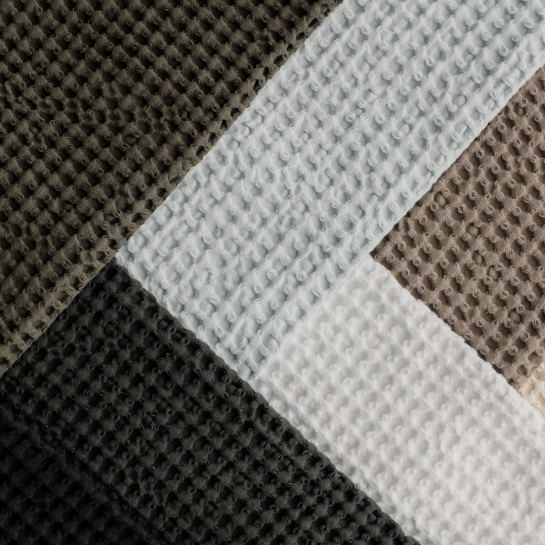 Nahaufnahme von strukturiertem Stoff in vier Farben: schwarz, grau, weiß und creme.