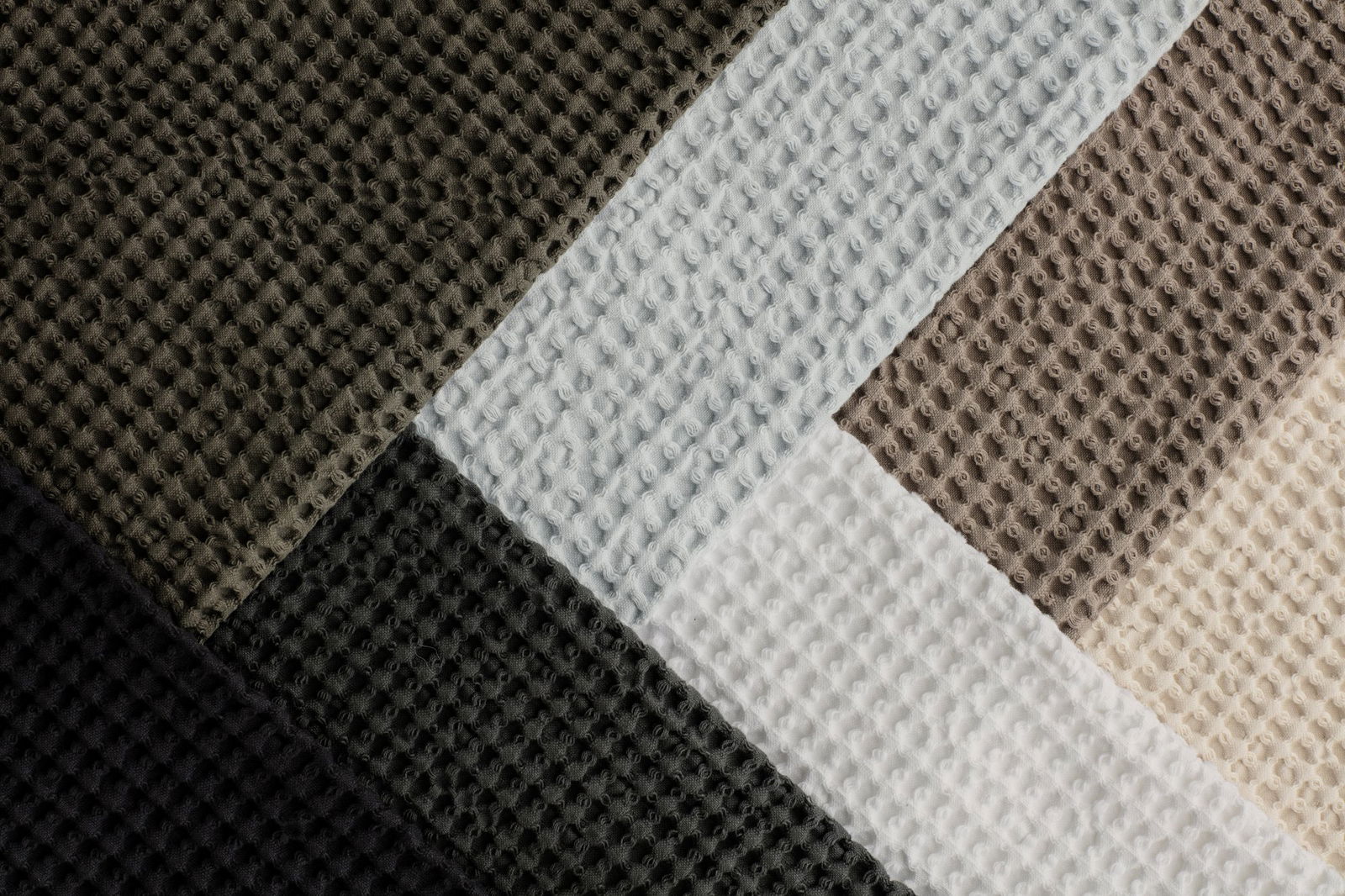 Nahaufnahme von strukturiertem Stoff in vier Farben: schwarz, grau, weiß und creme.
