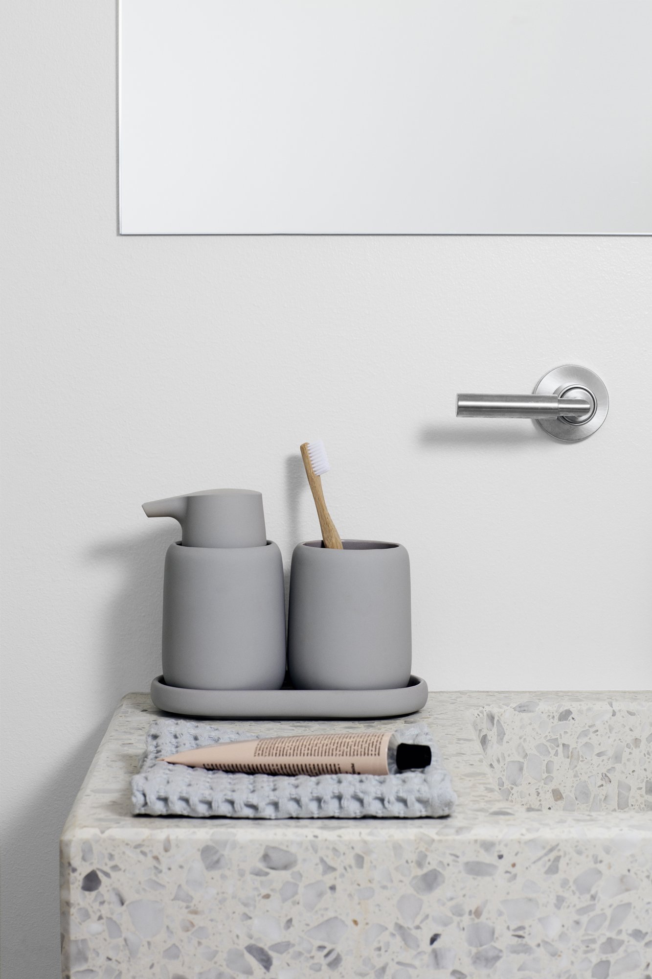 Moderne Badezimmer-Essentials mit grauen Keramikhaltern, einer Zahnbürste und einem dekorativen Tablett.