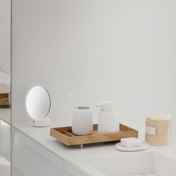 Minimalist bathroom decor featuring wooden tray, white containers, and a round mirror.