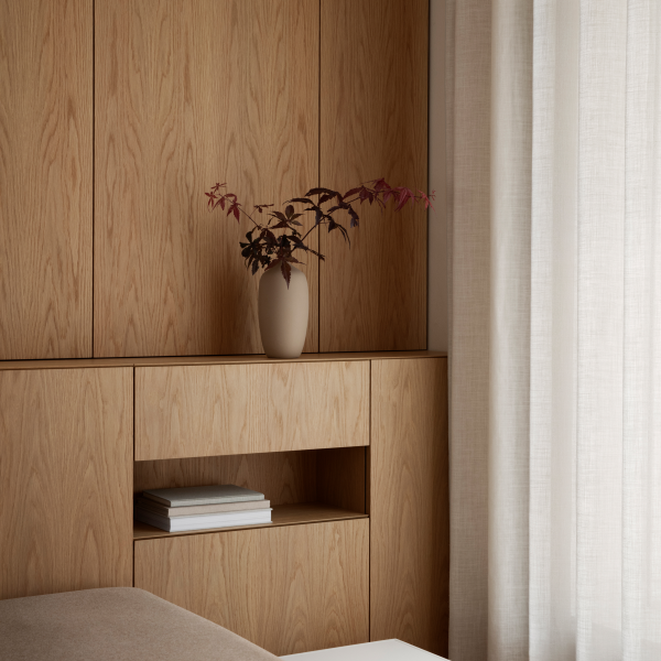 A minimalistic interior featuring a vase with leaves against a wooden backdrop and soft curtains.