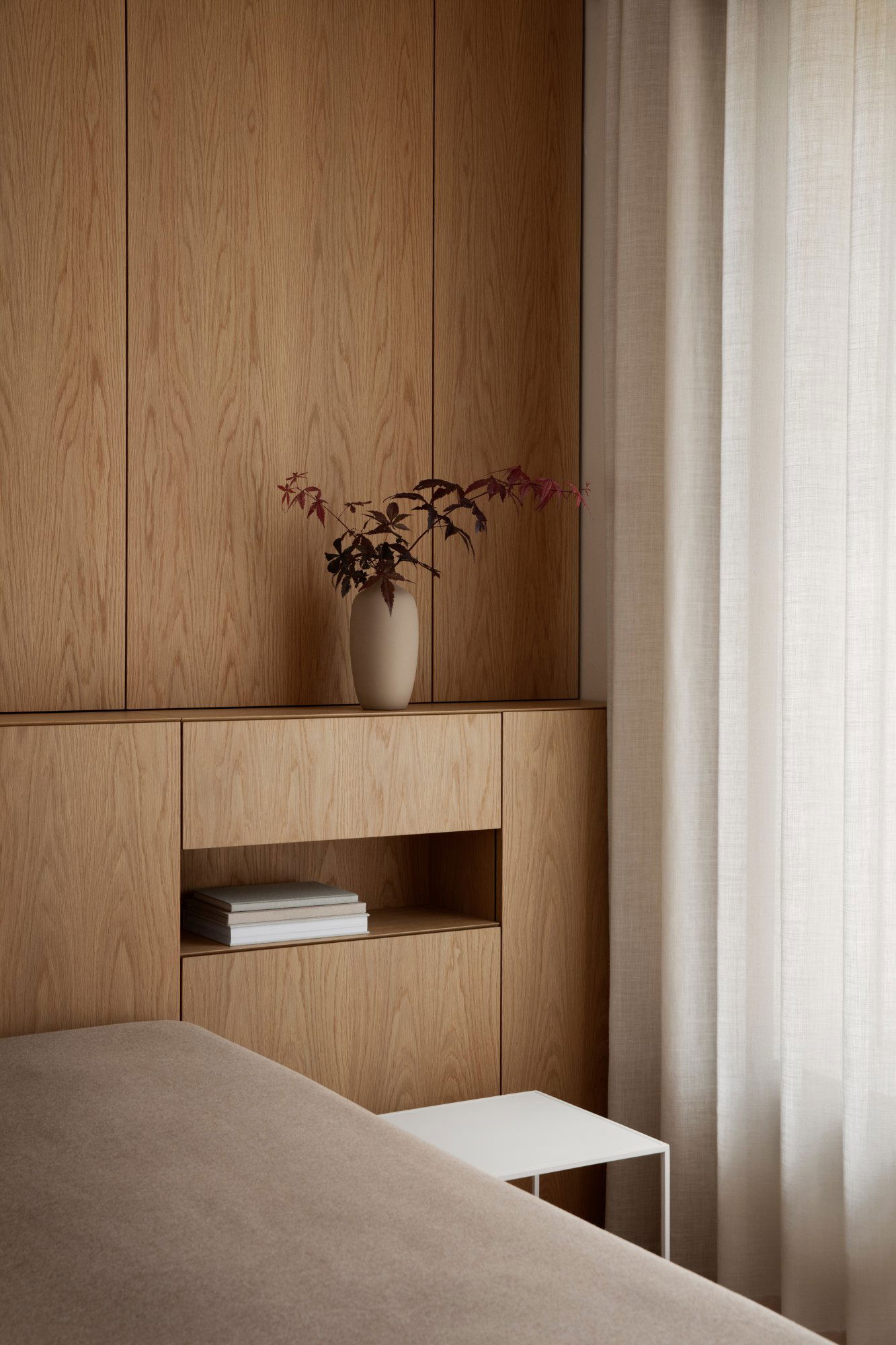 A minimalistic interior featuring a vase with leaves against a wooden backdrop and soft curtains.