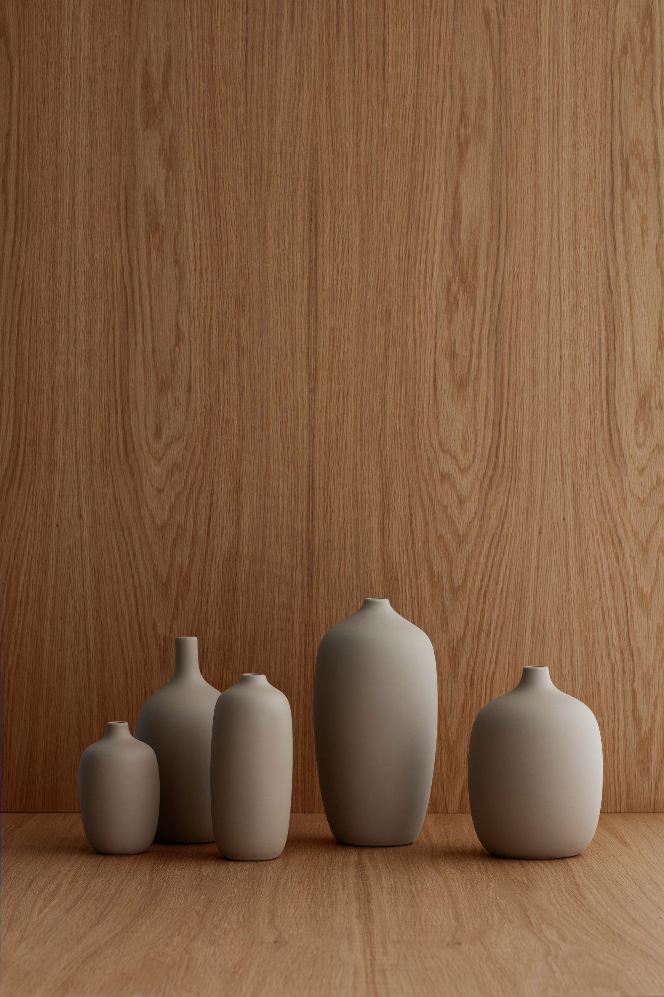 Minimalist vases in varying shapes against a textured wooden background.