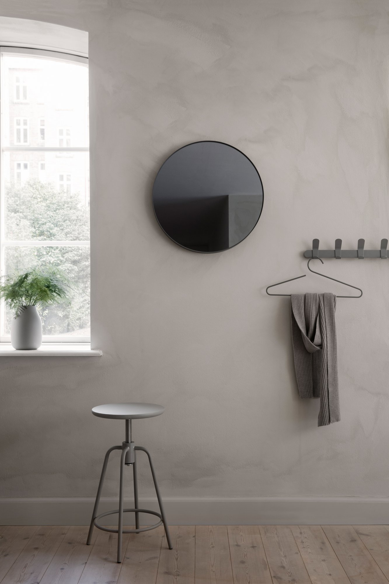 Moderne Innenraumdekoration mit einem runden Spiegel, einem Hocker und minimalistischen Wandhaken.