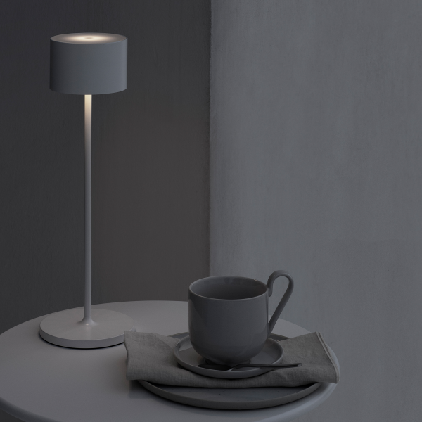 Modern gray lamp beside a cup and saucer on a minimalist table in soft lighting.