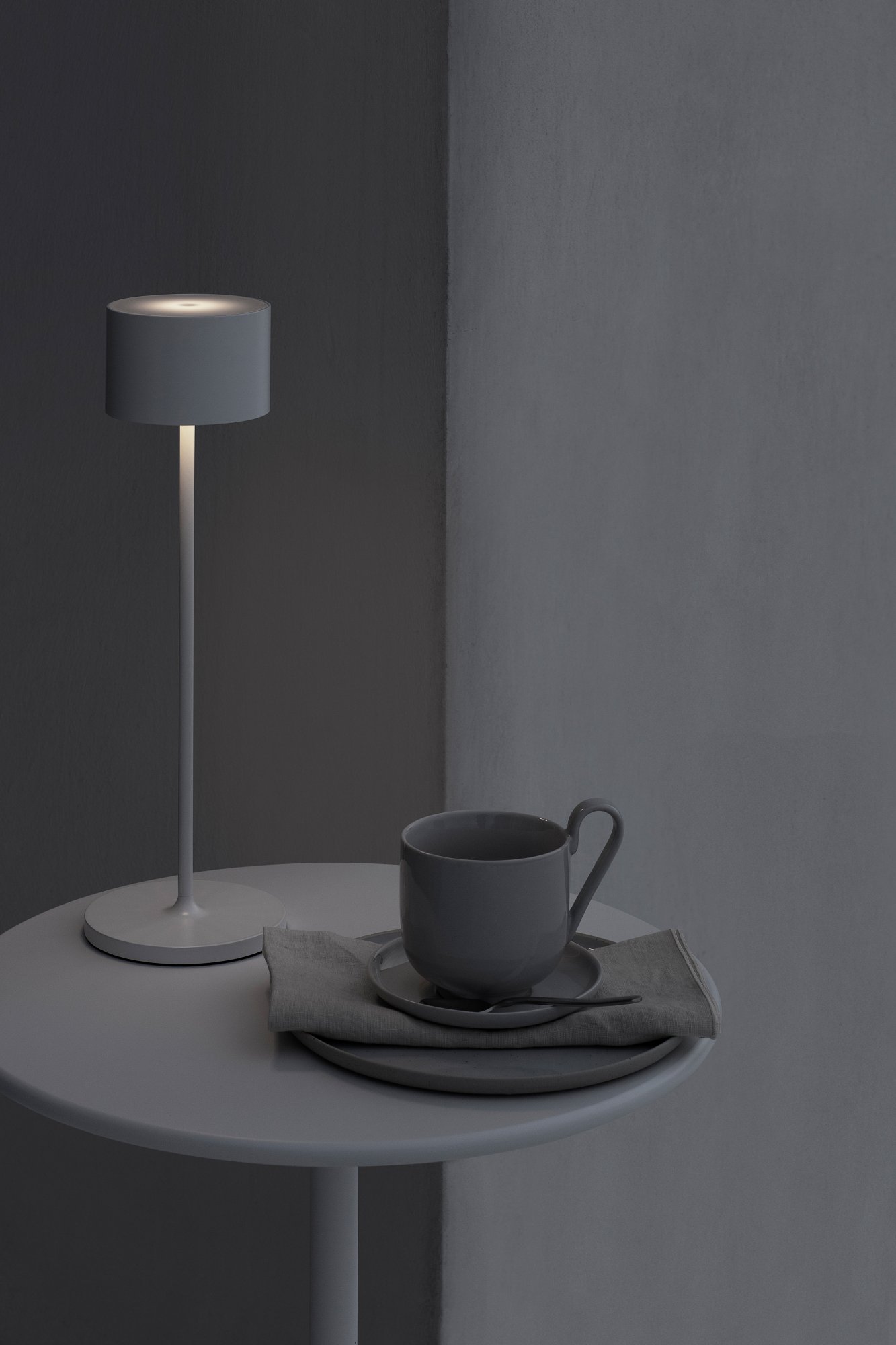 Modern gray lamp beside a cup and saucer on a minimalist table in soft lighting.