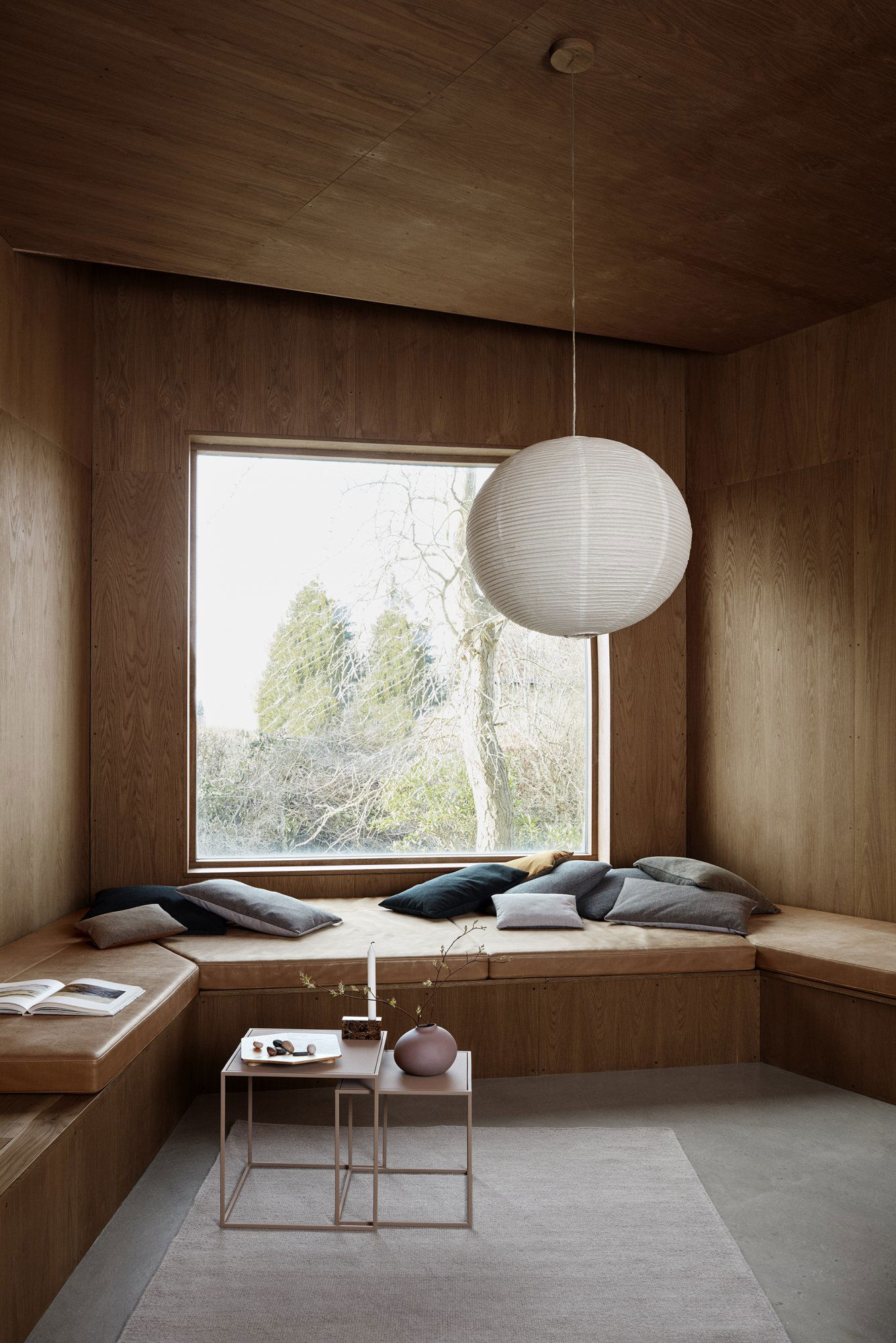 Gemütliche Ecke mit Kissen, natürlichem Licht und einer Papierlaterne in einem modernen Holzraum.