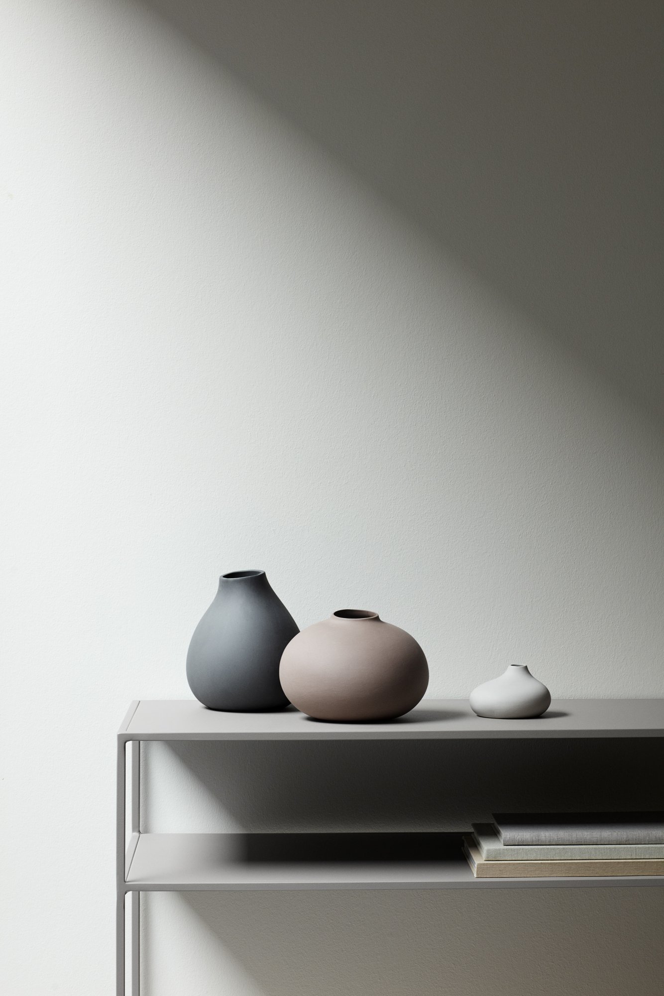 Elegant ceramic vases in neutral tones displayed on a minimalist shelf against a soft backdrop.