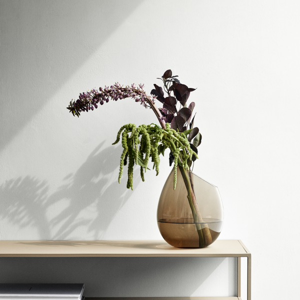 Elegant vase with lush green plants and purple flowers on a minimalist shelf.