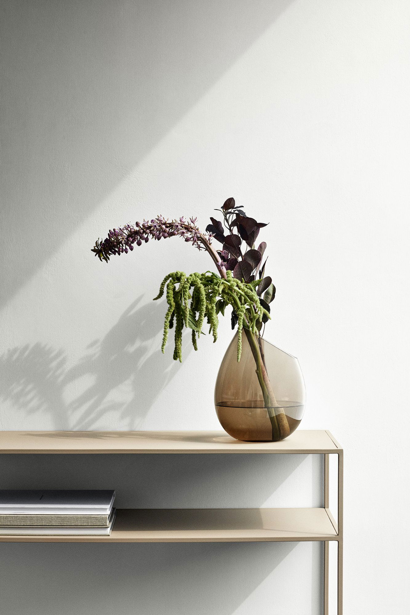 Elegant vase with lush green plants and purple flowers on a minimalist shelf.