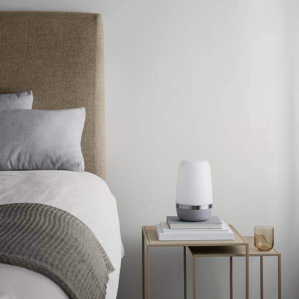 Gemütliche Schlafzimmer-Szene mit einer sanften Lampe auf einem Nachttisch neben einem ordentlich gemachten Bett.