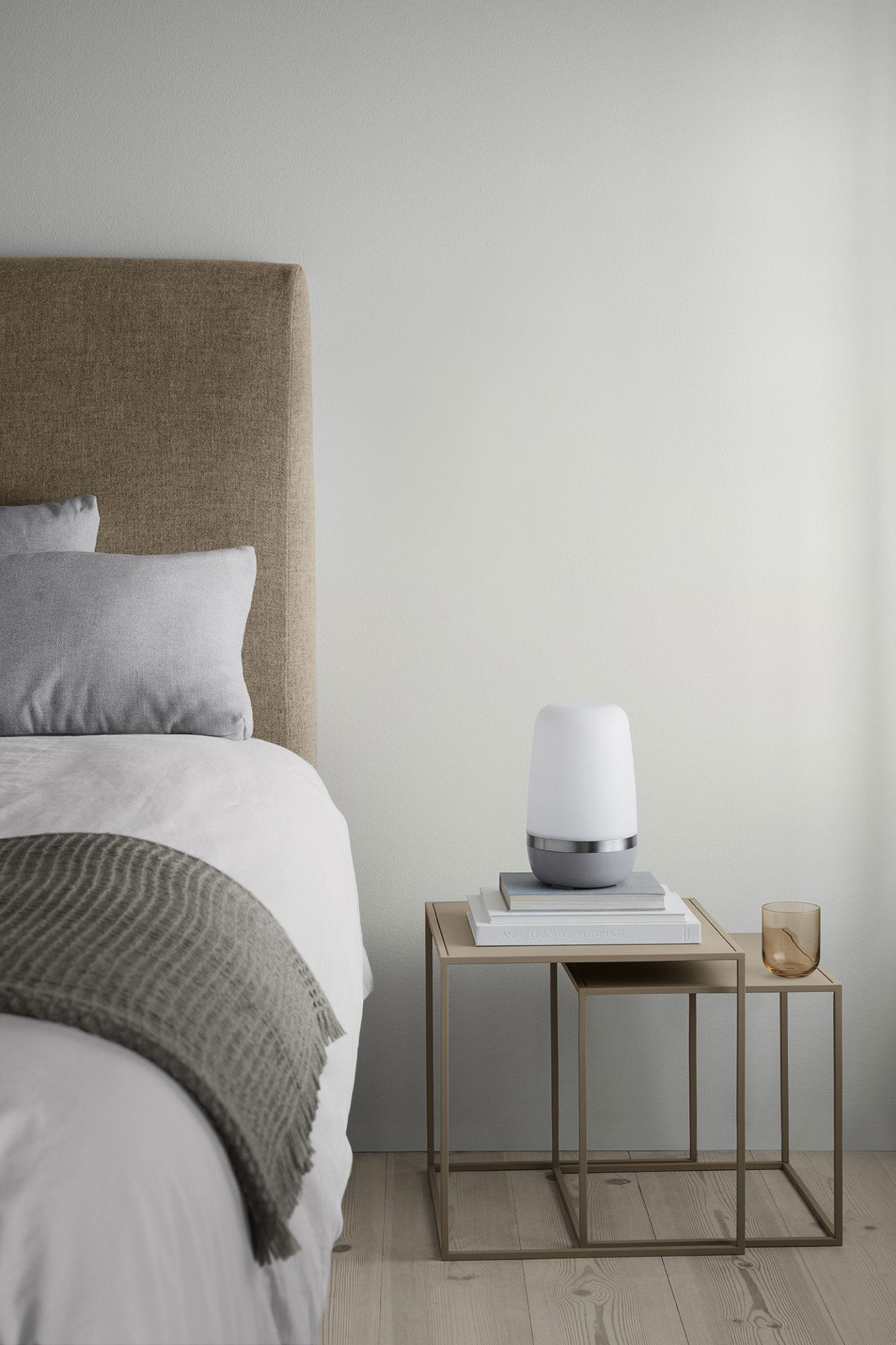 Gemütliche Schlafzimmer-Szene mit einer sanften Lampe auf einem Nachttisch neben einem ordentlich gemachten Bett.