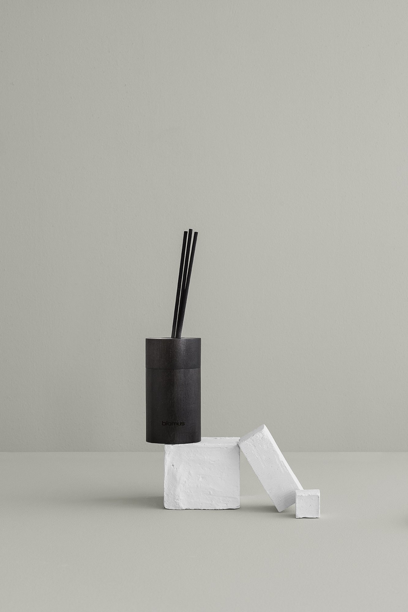 Stylischer schwarzer Diffusor auf weißen Blöcken vor einem minimalistischen grünen Hintergrund.
