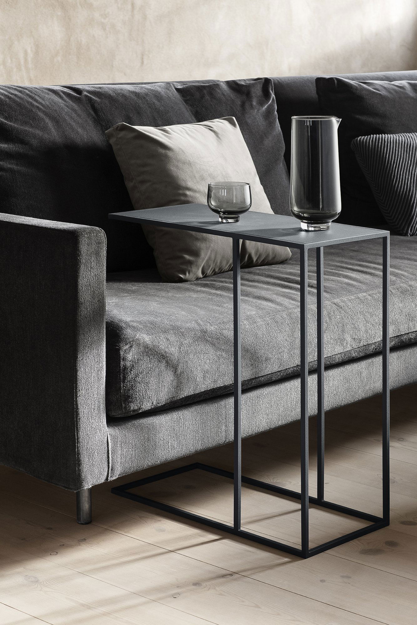 Stylischer moderner Beistelltisch mit Gläsern darauf neben einem gemütlichen grauen Sofa im Wohnzimmer.