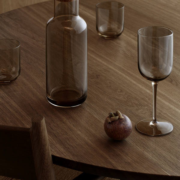 Elegante Holztischanordnung mit einer Glasflasche, einem gestielten Glas und dekorativen Früchten.