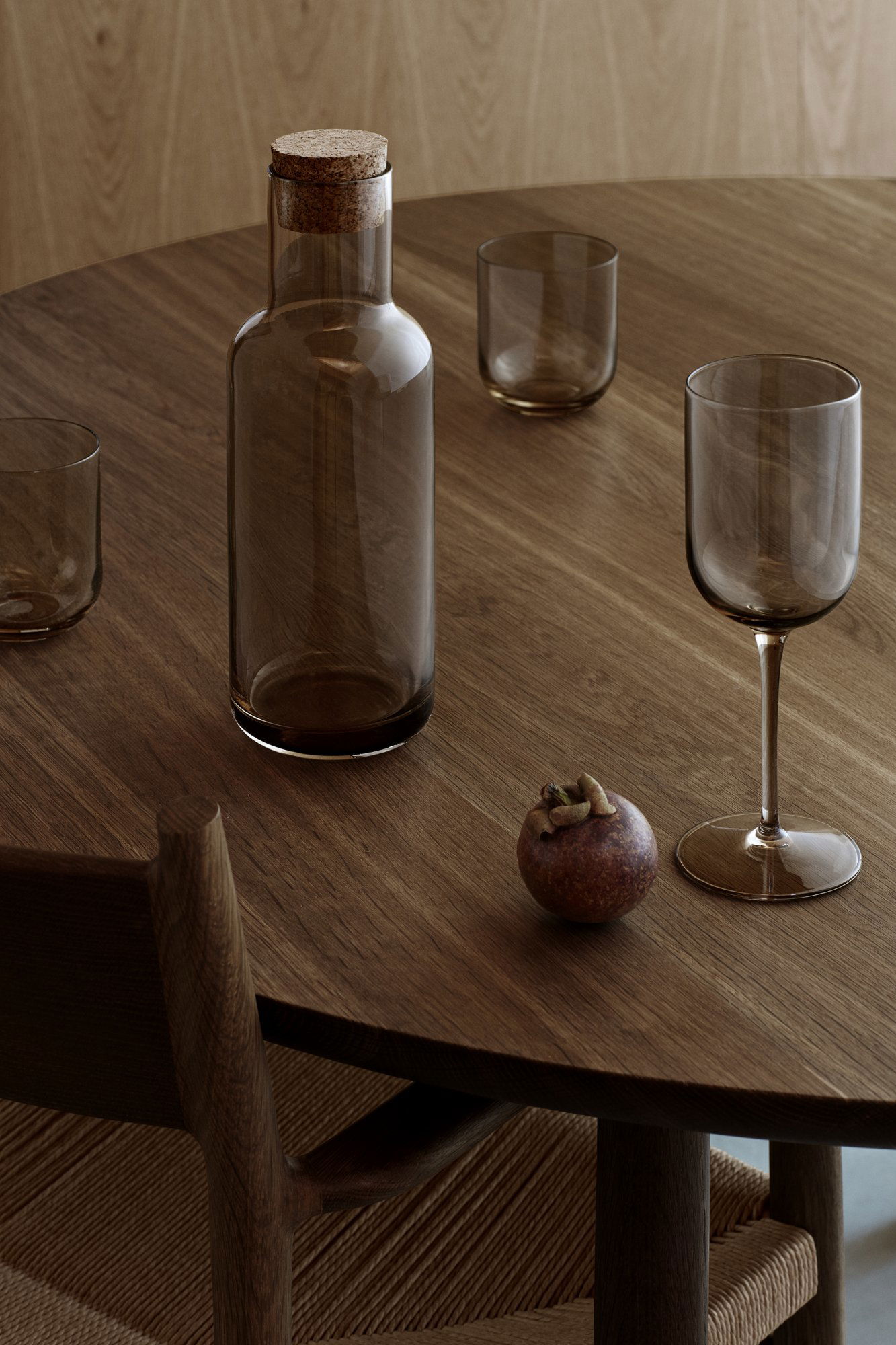 Elegante Holztischanordnung mit einer Glasflasche, einem gestielten Glas und dekorativen Früchten.