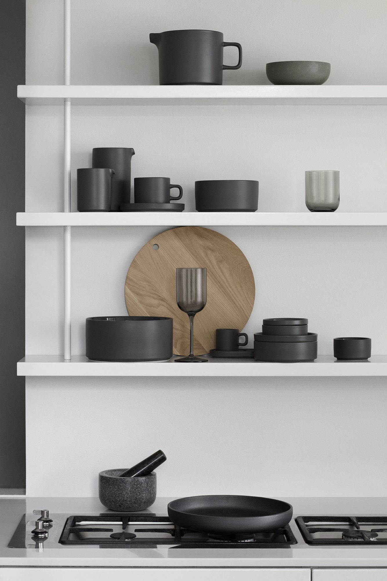 Moderne schwarze Keramikteller auf einem minimalistischen weißen Regal mit einem Holzelement präsentiert.