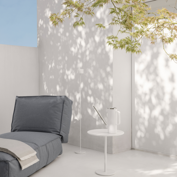 Cozy outdoor space with a gray lounge chair and minimalist decor under leafy shadows.