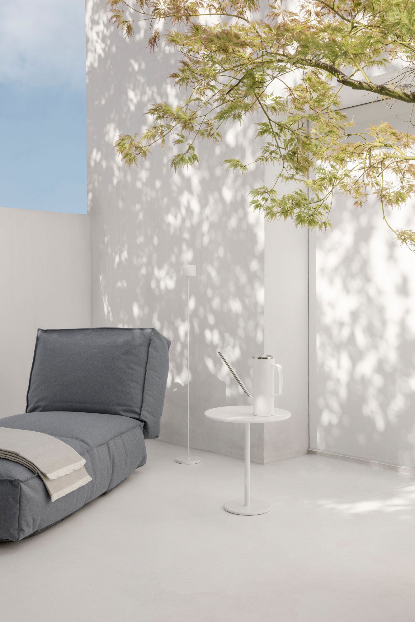 Cozy outdoor space with a gray lounge chair and minimalist decor under leafy shadows.
