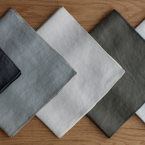 Assorted linen napkins in gray, white, and olive green arranged on a wooden surface.