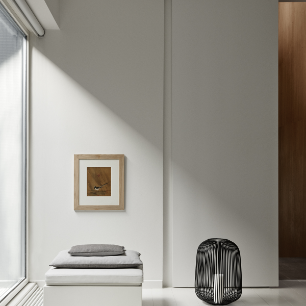 Minimalistische Inneneinrichtung mit einem gerahmten Kunstwerk, einem Kissen und einem modernen Drahthocker.