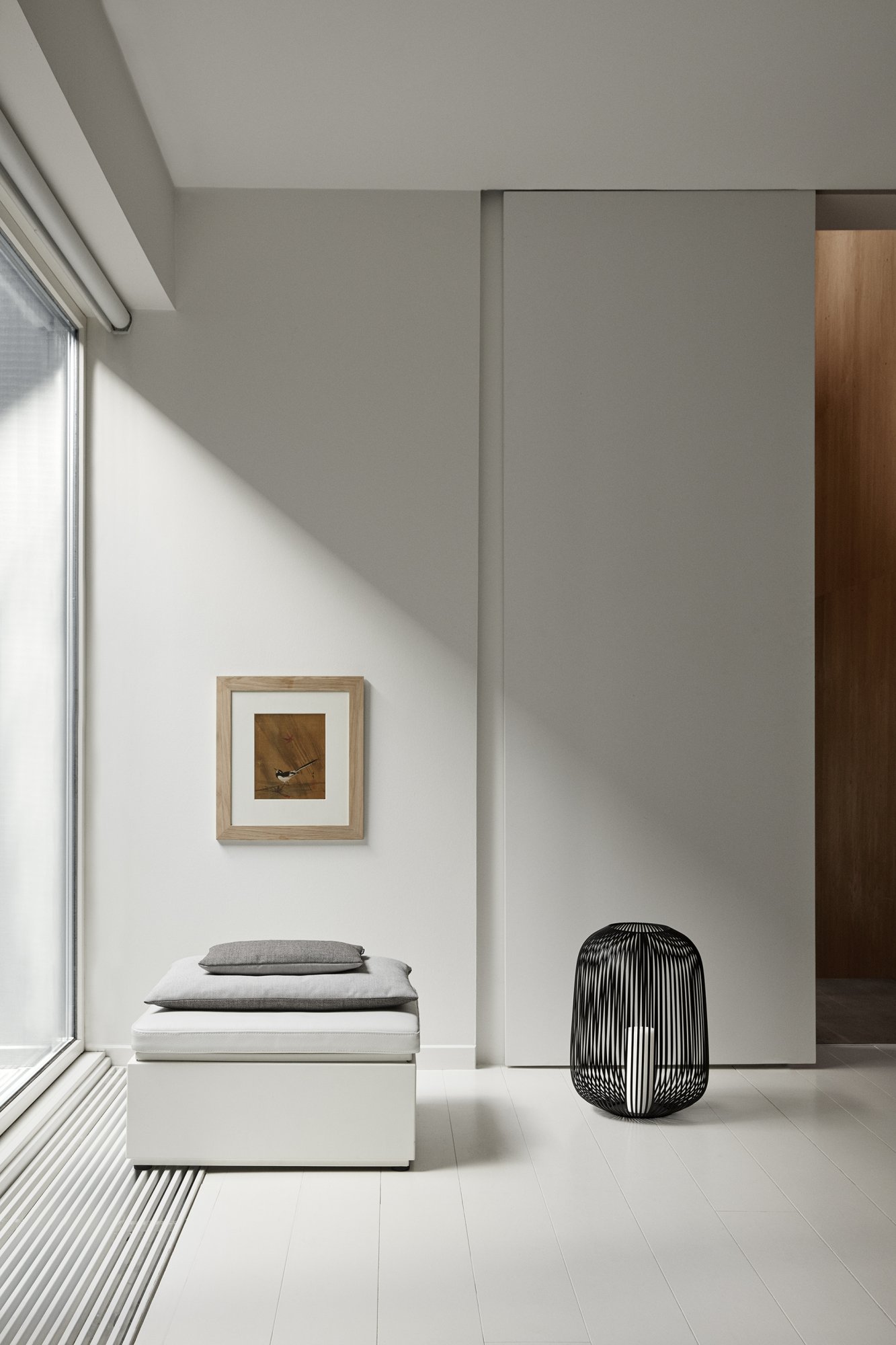 Minimalistische Inneneinrichtung mit einem gerahmten Kunstwerk, einem Kissen und einem modernen Drahthocker.