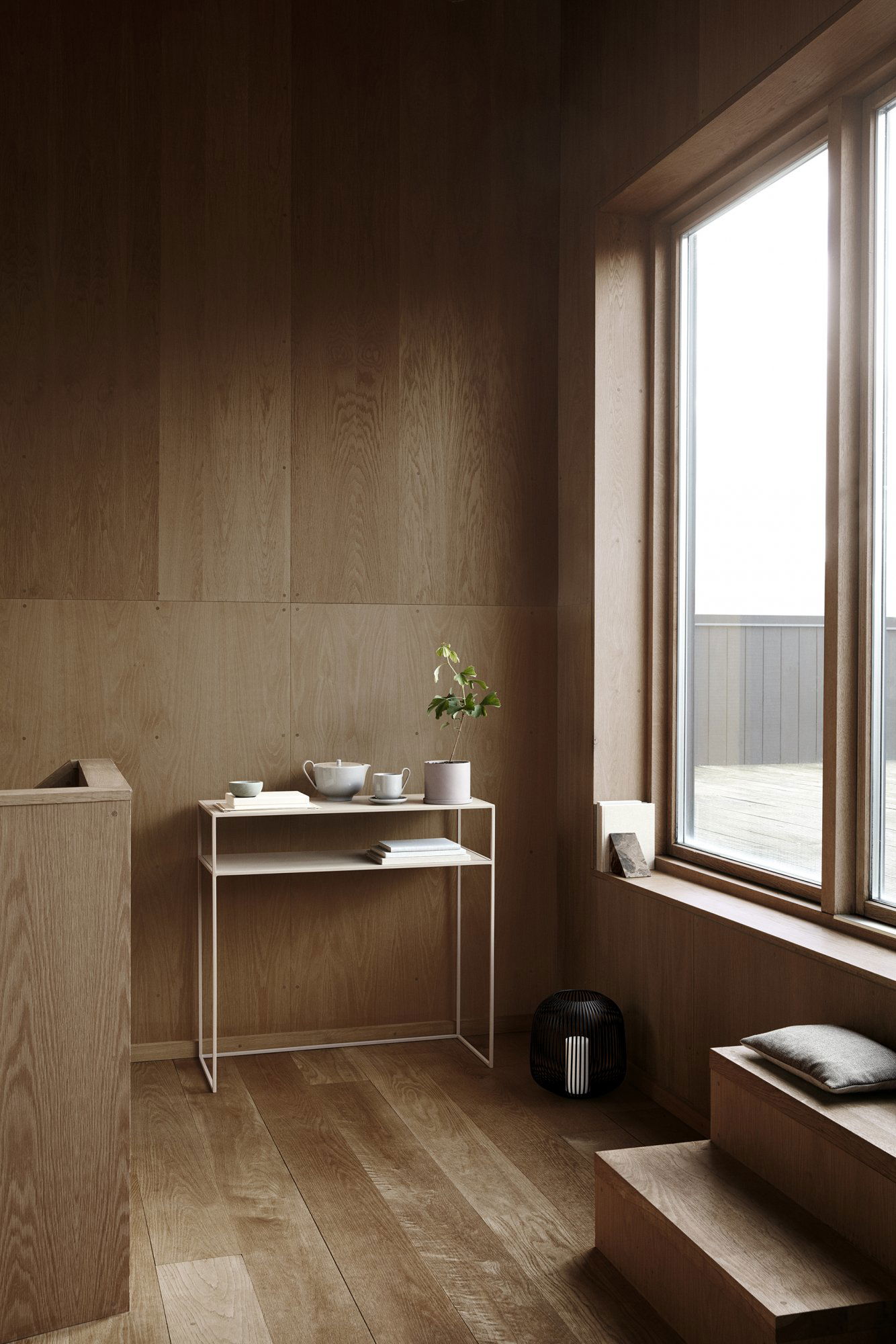 Minimalistisches Interieur mit Holzwänden, einem stilvollen Tisch und einer Topfpflanze neben einem großen Fenster.