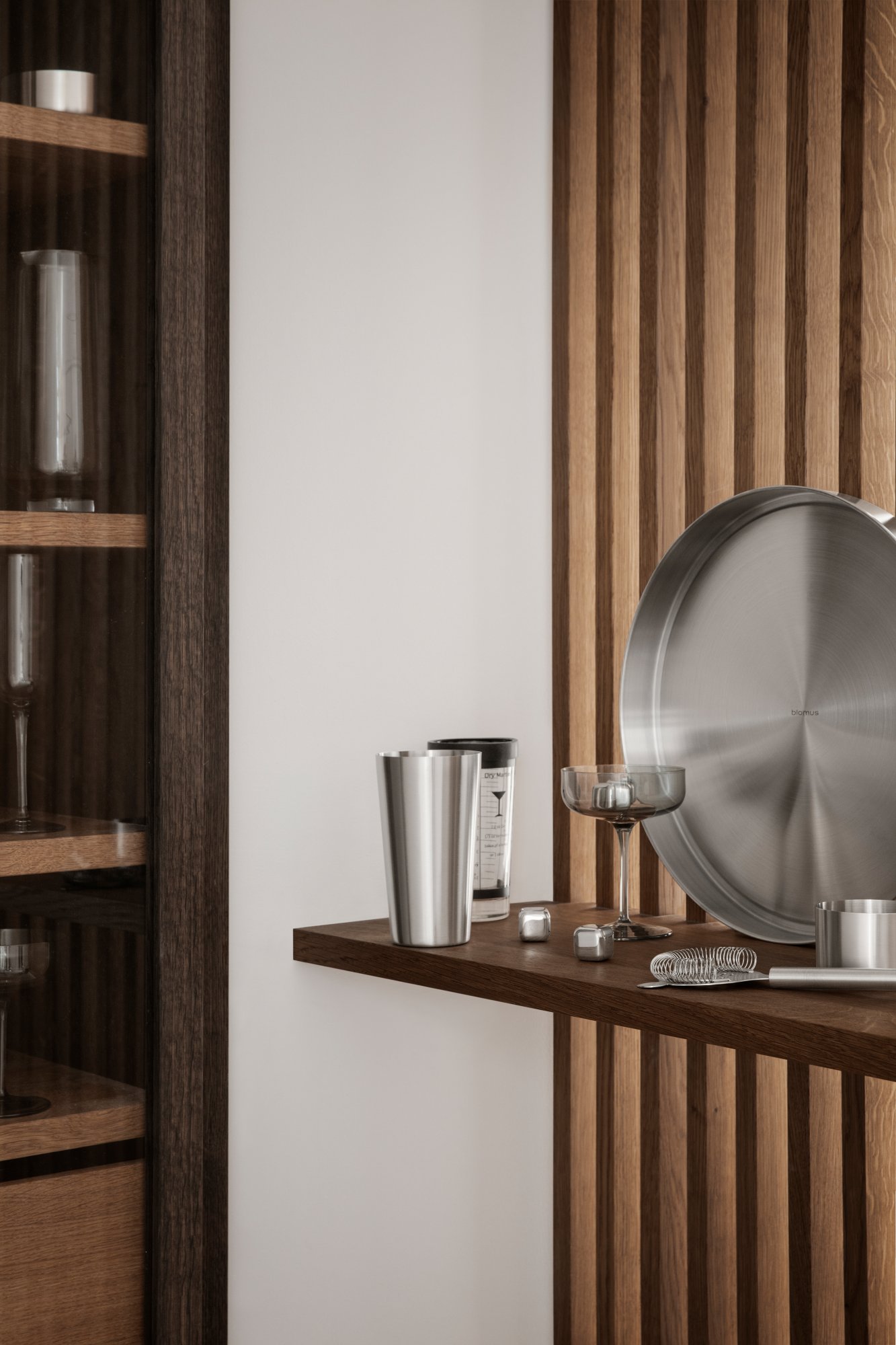 Moderne Küchenbar mit Edelstahlwerkzeugen und eleganten Gläsern auf Holzregalen.