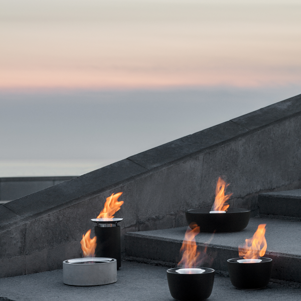 Moderne Feuerschalen, die die Außentreppe bei Sonnenuntergang am Meer beleuchten.