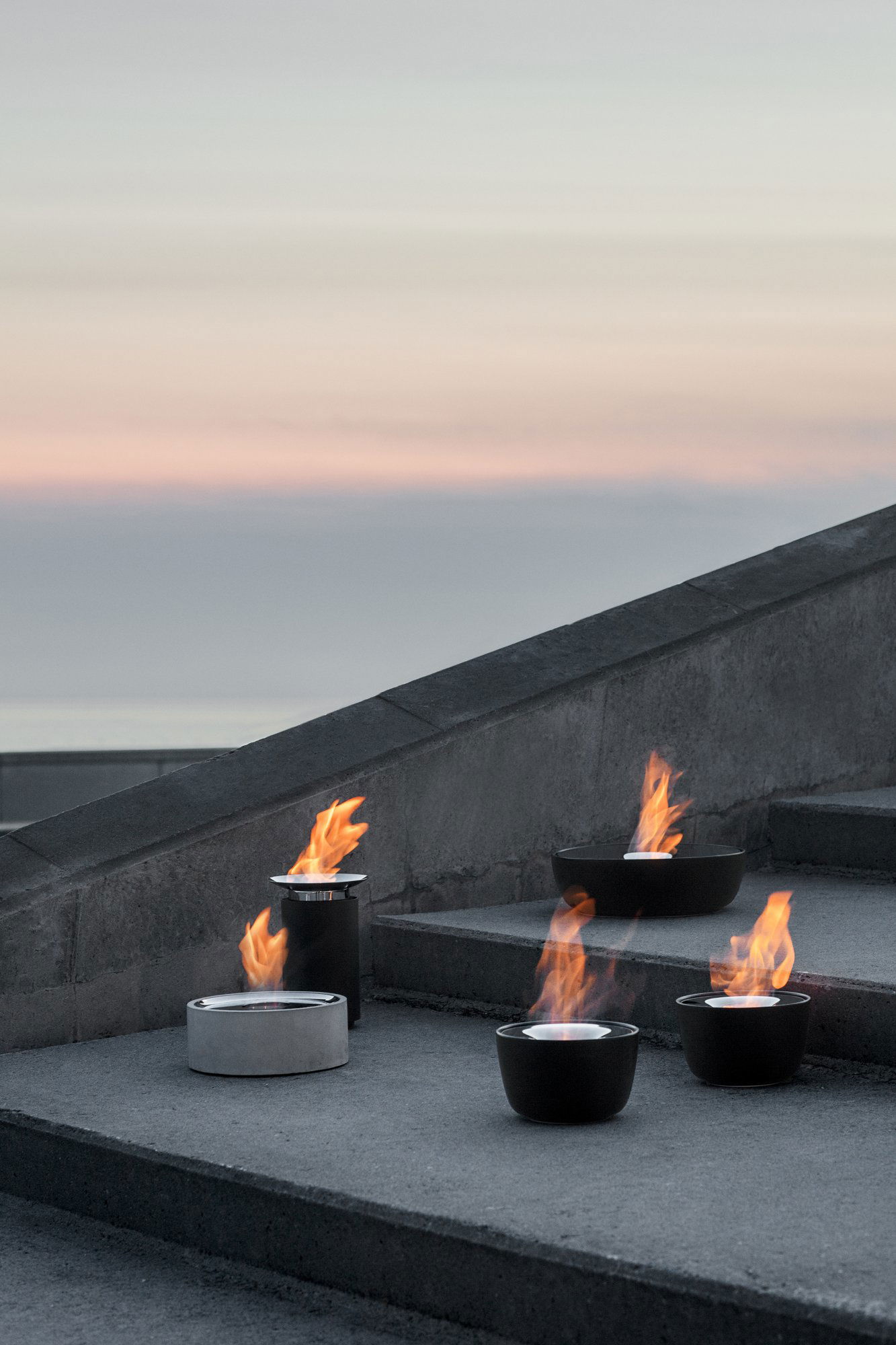 Moderne Feuerschalen, die die Außentreppe bei Sonnenuntergang am Meer beleuchten.