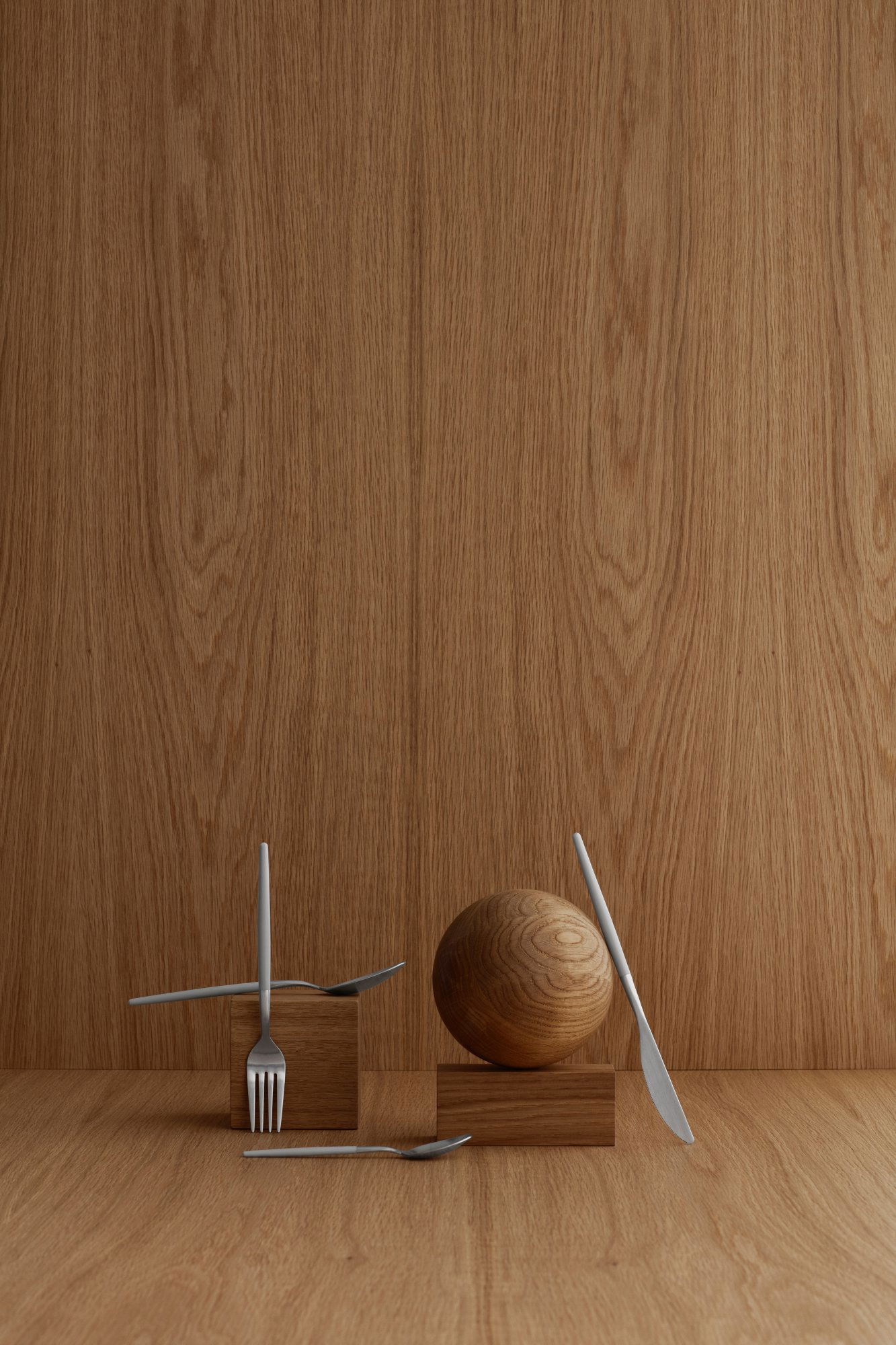 Minimalistische Kücheneinrichtung mit einer Gabel, einem Messer und einer Holzkugel vor einem Holzpaneel-Hintergrund.