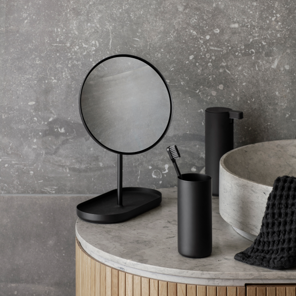 Stilvolle schwarze Badezimmeraccessoires mit einem Spiegel, einem Zahnbürstenhalter und einem Steingewässer.