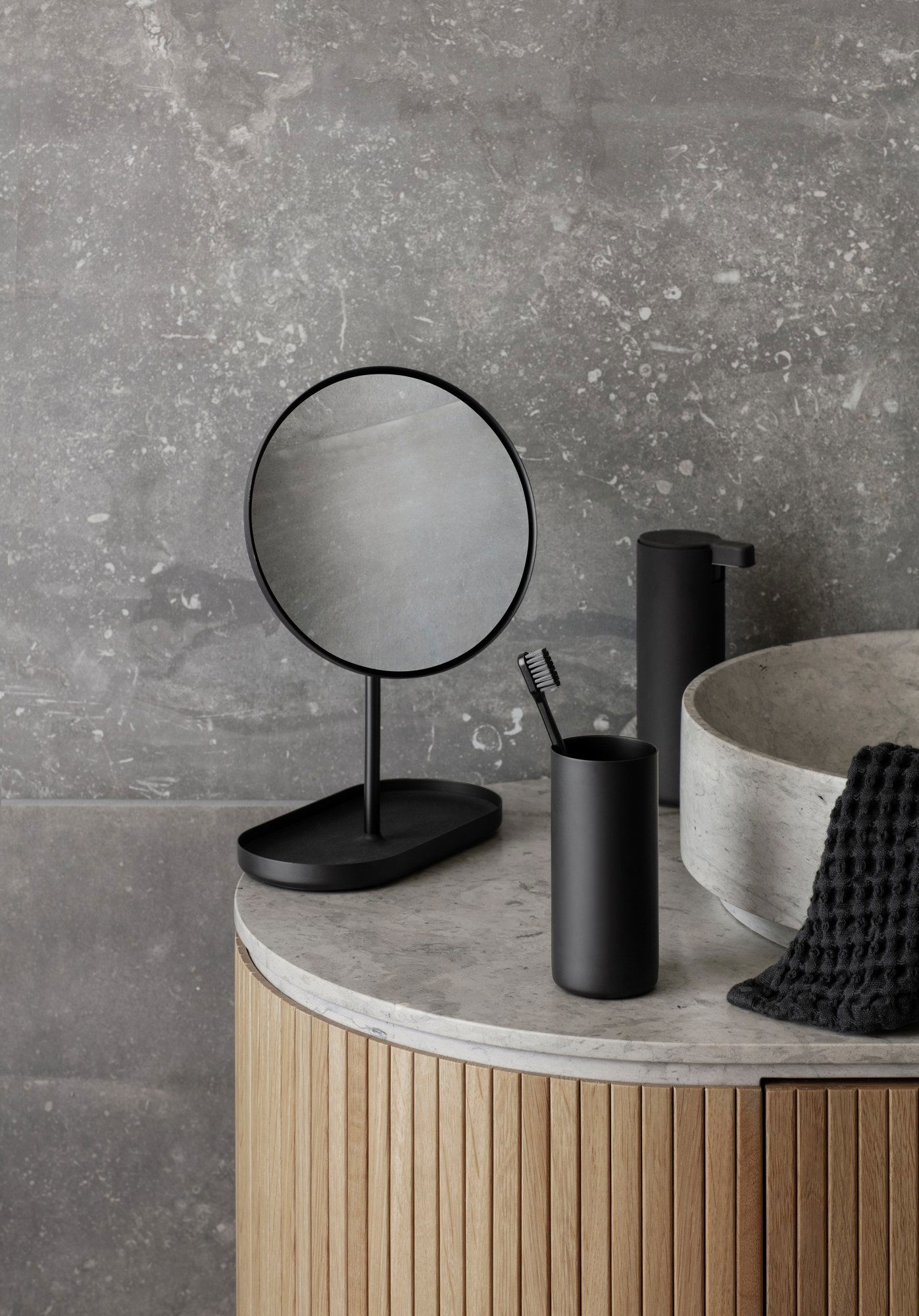 Stilvolle schwarze Badezimmeraccessoires mit einem Spiegel, einem Zahnbürstenhalter und einem Steingewässer.