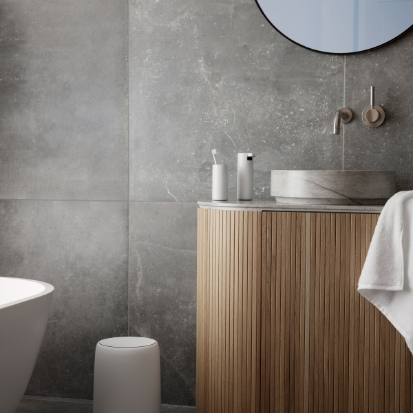 Modern bathroom with gray tiles, wooden vanity, circular mirror, and minimalist decor.
