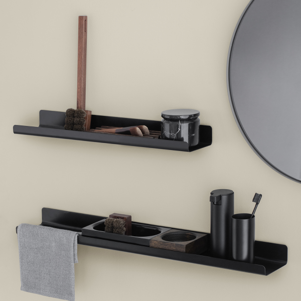 Stylische schwarze Badezimmerregale mit Toilettenartikeln und einem Spiegel an einer beigen Wand.
