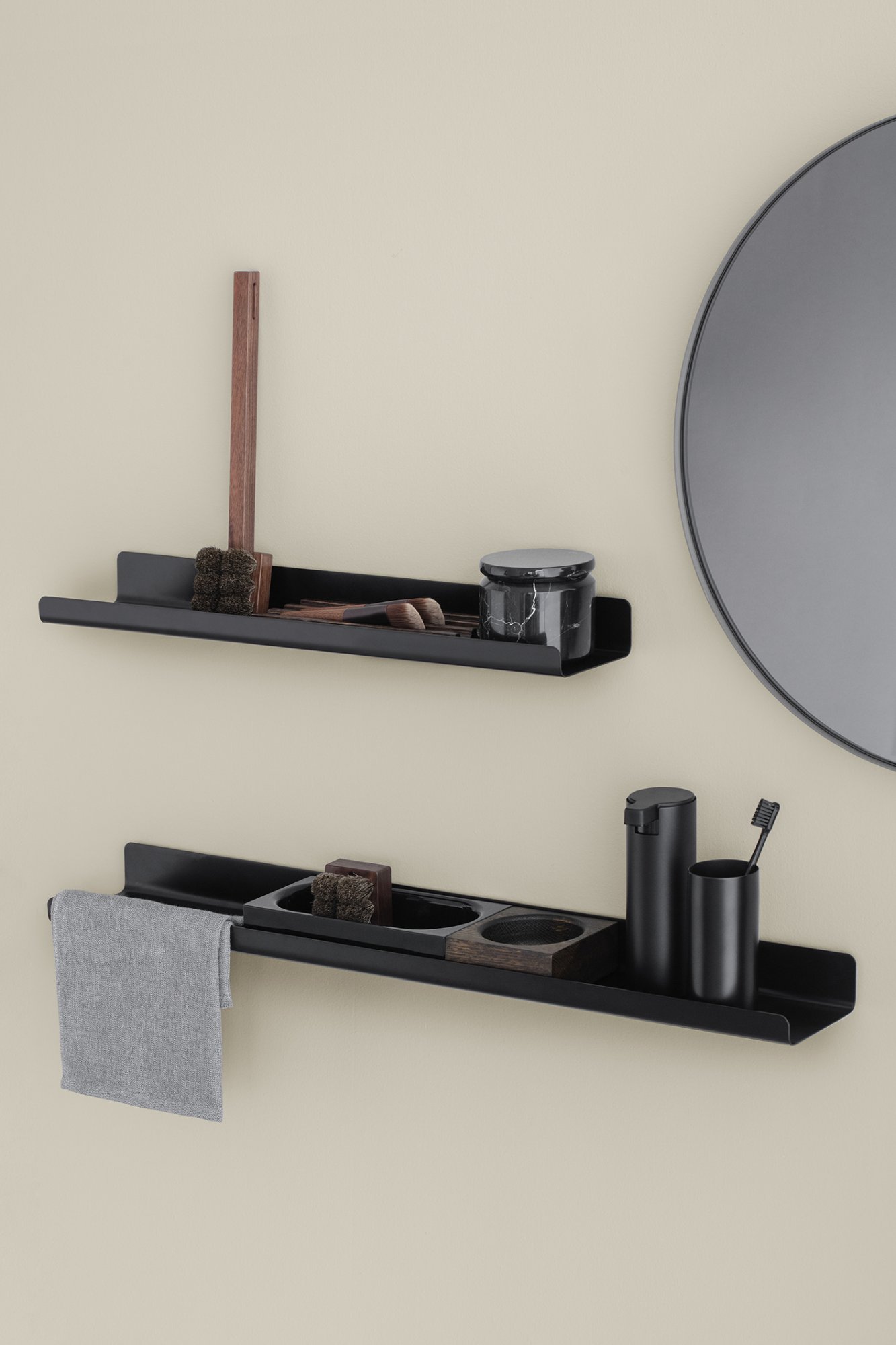 Stylische schwarze Badezimmerregale mit Toilettenartikeln und einem Spiegel an einer beigen Wand.