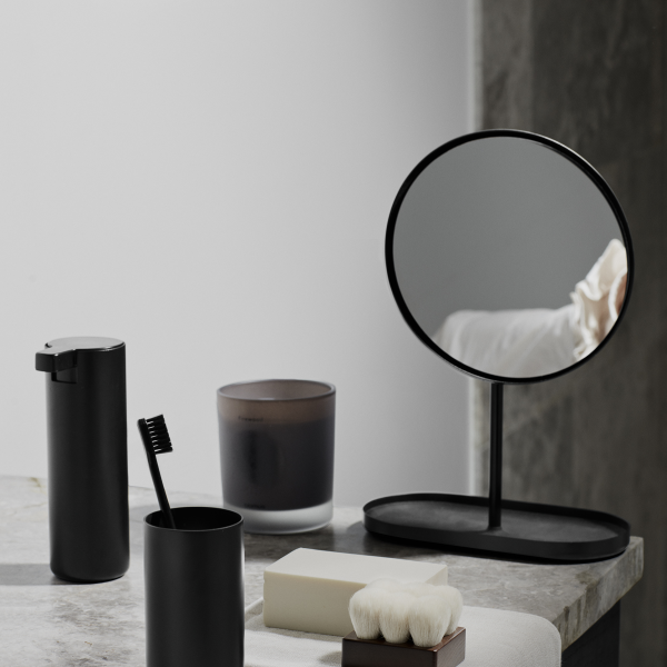 Moderne Badezimmer-Einrichtung mit schwarzen Accessoires und einem runden Spiegel.