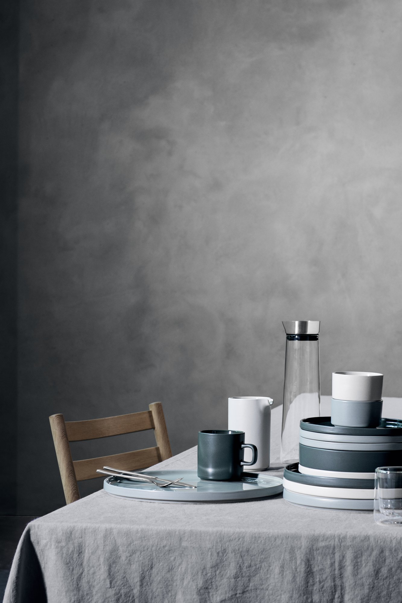 Modernes Ess-Setup mit minimalistischem Geschirr, darunter Tassen und Behälter, vor einem strukturierten Hintergrund.