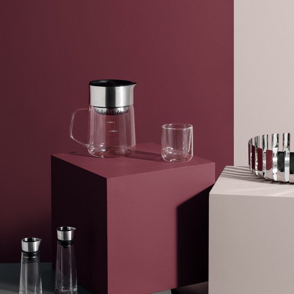 Moderne Glas-Kaffeemaschine und Tasse auf minimalistischem, farblich abgesetztem Display.