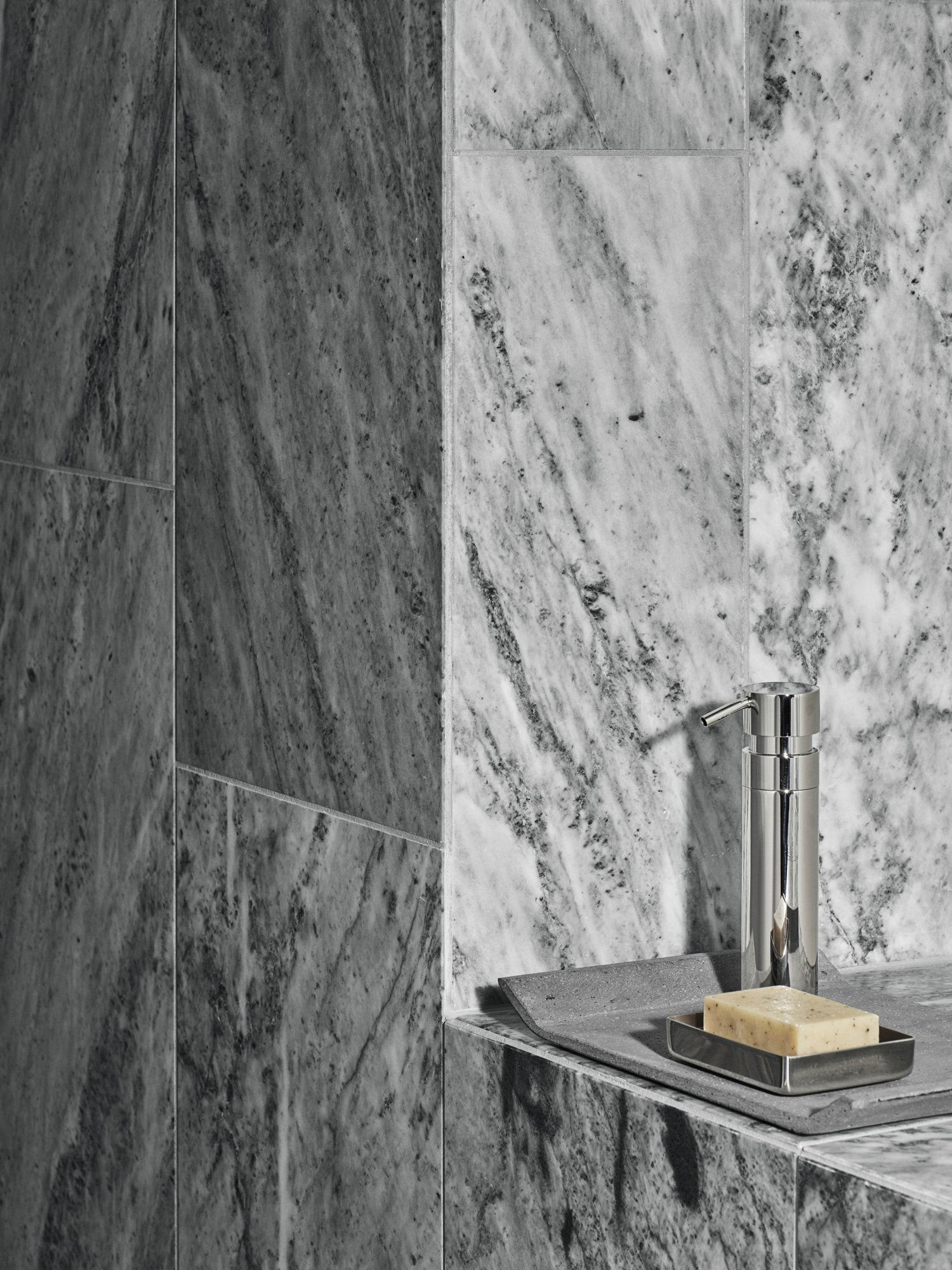 Sleek modern bathroom with marble walls and stylish soap dispenser on a countertop.