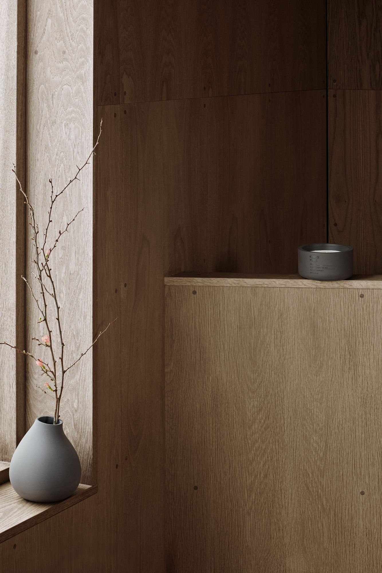 Minimalistische Einrichtung mit Holzregalen und einer einfachen Vase mit Zweigen.