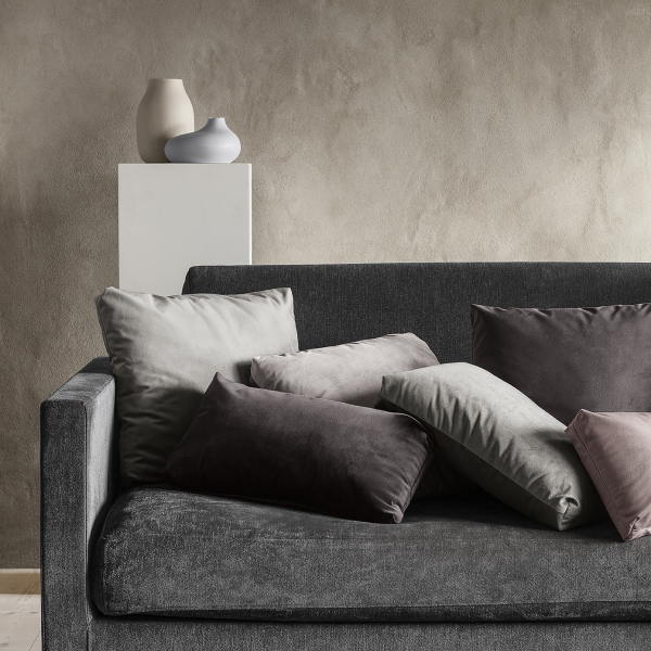 Gemütliche Wohnzimmer-Szene mit Kissen auf einem modernen grauen Sofa und dekorativen Vasen auf einem Regal.