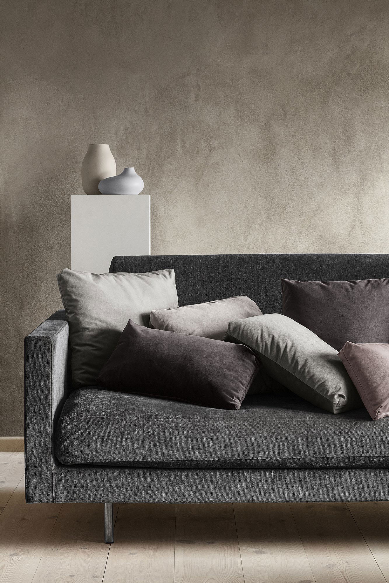 Gemütliche Wohnzimmer-Szene mit Kissen auf einem modernen grauen Sofa und dekorativen Vasen auf einem Regal.